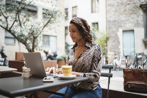 Junge Frau mit Laptop in einem Straßencafé - JPIF00450
