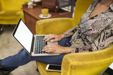 Close-up of young woman sitting in armchair using laptop - JPIF00458