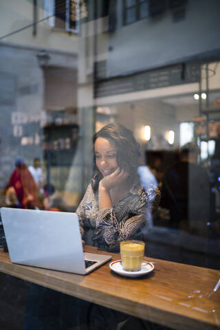 Young woman using laptop in a cafe behind windowpane stock photo