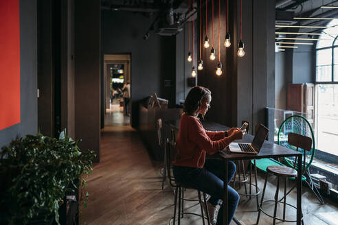 Young woman using laptop and smartphone in a cafe - JPIF00483