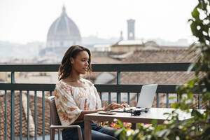 Junge Frau mit Laptop auf einem Balkon in Florenz, Italien - JPIF00494