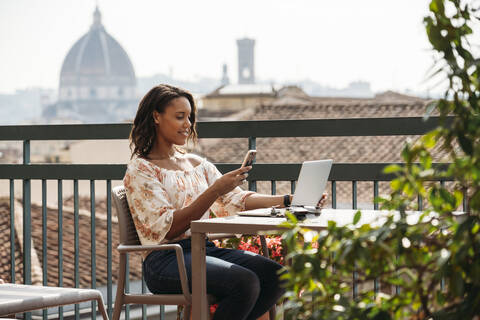 Junge Frau mit Laptop und Smartphone auf einem Balkon in Florenz, Italien, lizenzfreies Stockfoto