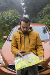 Mann mit Smartphone und Karte vor Auto auf Waldweg, Insel Sao Miguel, Azoren, Portugal - AFVF05667
