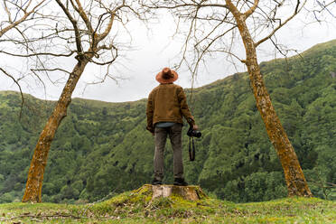 Rückansicht eines Mannes mit Kamera auf einem Baumstumpf, Insel Sao Miguel, Azoren, Portugal - AFVF05669