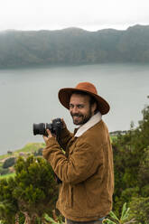 Portrait of smiling man with camera standing at a lake, Sao Miguel Island, Azores, Portugal - AFVF05673