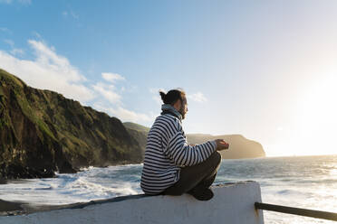 Mann meditiert an der Küste bei Sonnenuntergang, Insel Sao Miguel, Azoren, Portugal - AFVF05698