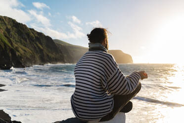 Mann meditiert an der Küste bei Sonnenuntergang, Insel Sao Miguel, Azoren, Portugal - AFVF05699