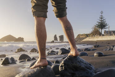 Beine eines Mannes, der auf Steinen am Strand steht, Insel Sao Miguel, Azoren, Portugal - AFVF05706