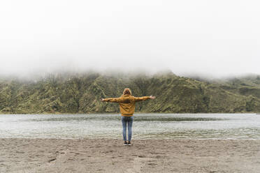 Full length of female tourist with arms outstretched standing at lakeshore in Sao Miguel Island, Azores, Portugal - AFVF05711