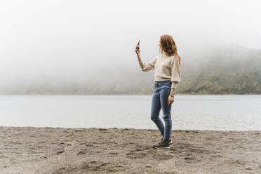 Frau beim Fotografieren am Seeufer während der Erkundung der Insel Sao Miguel, Azoren, Portugal - AFVF05717