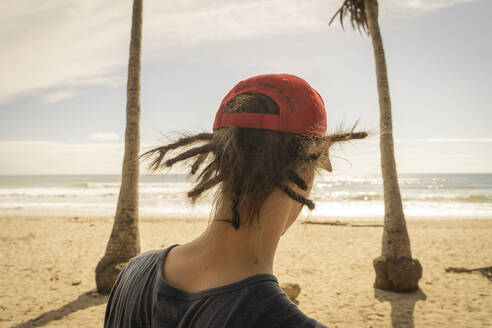 Costa Rica, Puntarenas Province, Puntarenas, Rear view of young man wearing dreadlocks looking at ocean from Playa Santa Teresa - TEBF00036