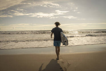 Costa Rica, Provinz Puntarenas, Puntarenas, Rückansicht eines männlichen Surfers, der mit einem Surfbrett in der Hand auf das Meer zugeht - TEBF00037