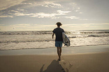 Costa Rica, Puntarenas Province, Puntarenas, Rear view of male surfer walking toward ocean with surfboard in hand - TEBF00037