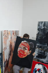 Eine Malerin versteckt sich hinter einem Bild in ihrem Atelier - OGF00234