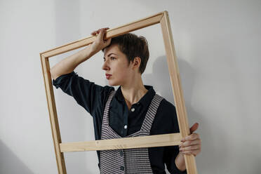 Porträt einer Malerin, die einen Bilderrahmen in ihrem Atelier hält - OGF00256