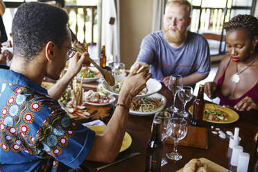 Multiethnische Freunde essen zu Mittag, während sie am Esstisch sitzen - VEGF01737
