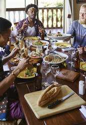 Multi-ethnic friends eating lunch while sitting at dining table in room - VEGF01739