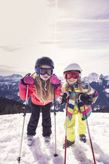 Excited sisters with skis standing on snow covered mountain in winter at Spitzingsee, Bavaria, Germany - DHEF00154