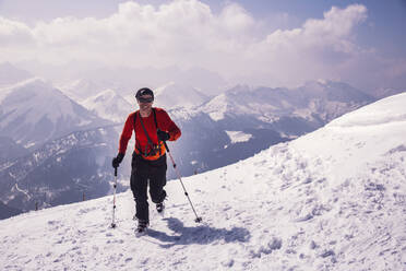 Full length of happy man running with skis on snow covered mountain at Achenkirch, Tyrol, Austria - DHEF00159