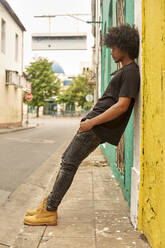 Junger Mann mit Afro, der sich in der Stadt an eine Wand lehnt - VEGF01755