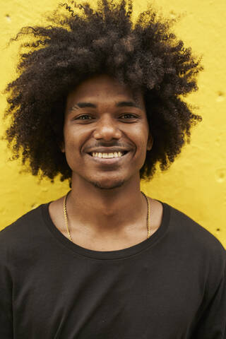 Porträt eines glücklichen jungen Mannes mit Afro gegen eine gelbe Wand, lizenzfreies Stockfoto