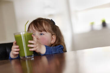 Portrait of toddler girl taking glass of green smoothie - AUF00160