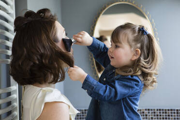 Mädchen im Kleinkindalter trägt Make-up auf das Gesicht ihrer Mutter auf - AUF00161