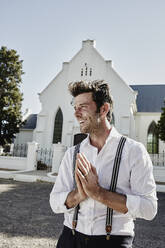 Happy man in old-fashioned clothes in the countryside praying at a church - RORF02030