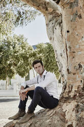 Man in old-fashioned clothes sitting at a tree in the countryside - RORF02040