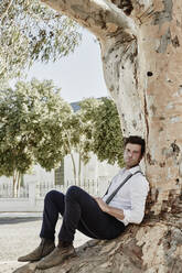 Portrait of man in old-fashioned clothes sitting at a tree in the countryside - RORF02041