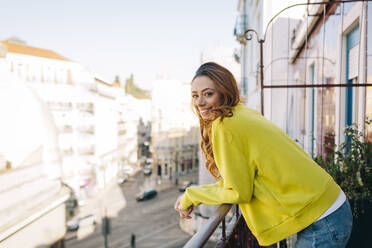 Porträt einer glücklichen jungen Frau, die auf einem Balkon steht - DCRF00144