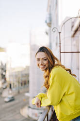 Porträt einer glücklichen jungen Frau, die auf einem Balkon steht - DCRF00145