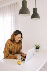 Junge Frau mit Laptop auf dem Tisch zu Hause - DCRF00149