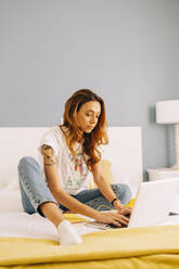 Young woman using laptop on bed at home - DCRF00151