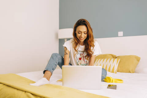 Junge Frau mit Laptop auf dem Bett zu Hause, lizenzfreies Stockfoto