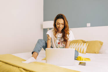 Junge Frau mit Laptop auf dem Bett zu Hause - DCRF00152