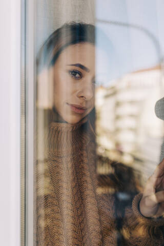 Porträt einer jungen Frau hinter einer Fensterscheibe, lizenzfreies Stockfoto