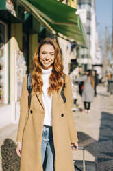 Portrait of happy young woman with baggage in the city, Lisbon, Portugal - DCRF00177