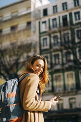 Porträt einer glücklichen jungen Frau mit Rucksack in der Stadt, Lissabon, Portugal - DCRF00179