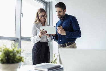 Businessman and woman working toghether in office, using digital tablet - JSRF00897