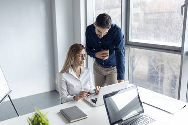 Businessmwoman sitting at desk, discussing work with her colleague - JSRF00912