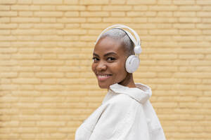 Porträt einer lächelnden Frau, die im Freien mit Kopfhörern Musik hört - AFVF05728