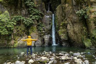 Mann steht mit ausgestreckten Armen vor einem Wasserfall, Sao Miguel, Azoren, Portugal - AFVF05755