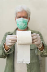 Mann mit Gesichtsmaske und Schutzhandschuhen, hält eine Rolle Toilettenpapier - AFVF05770