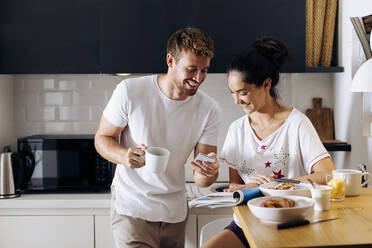 Happy young couple in the kitchen looking at cell phone - SODF00694