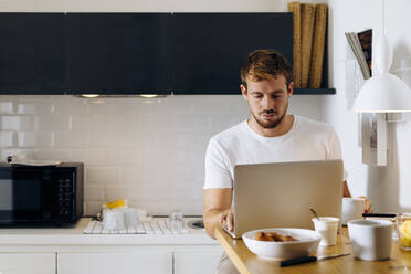 Young man using laptop in kitchen - SODF00700