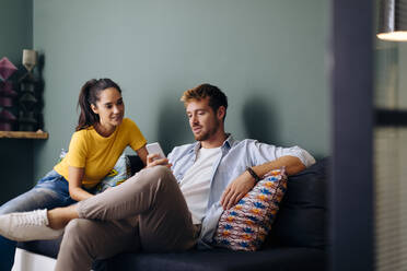 Junges Paar sitzt zu Hause auf der Couch und schaut auf sein Smartphone - SODF00701