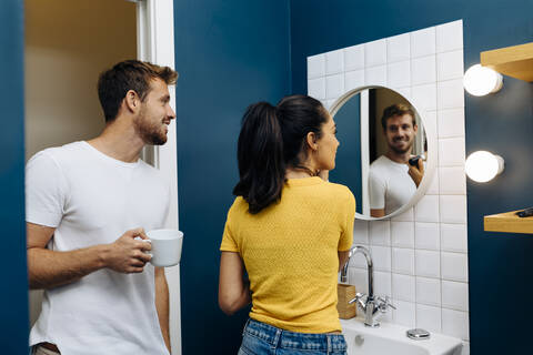 Lächelnder junger Mann beobachtet seine Freundin beim Auftragen von Make-up, lizenzfreies Stockfoto