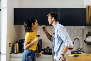 Glückliches junges Paar kocht und trinkt Wein in der Küche zu Hause zusammen - SODF00708