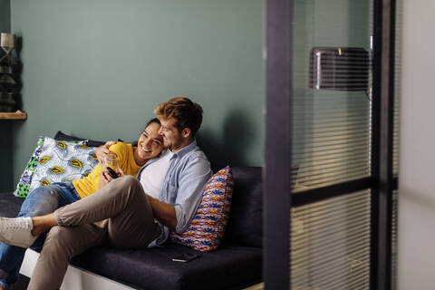 Glückliches, zärtliches, junges Paar, das zu Hause auf der Couch sitzt, lizenzfreies Stockfoto